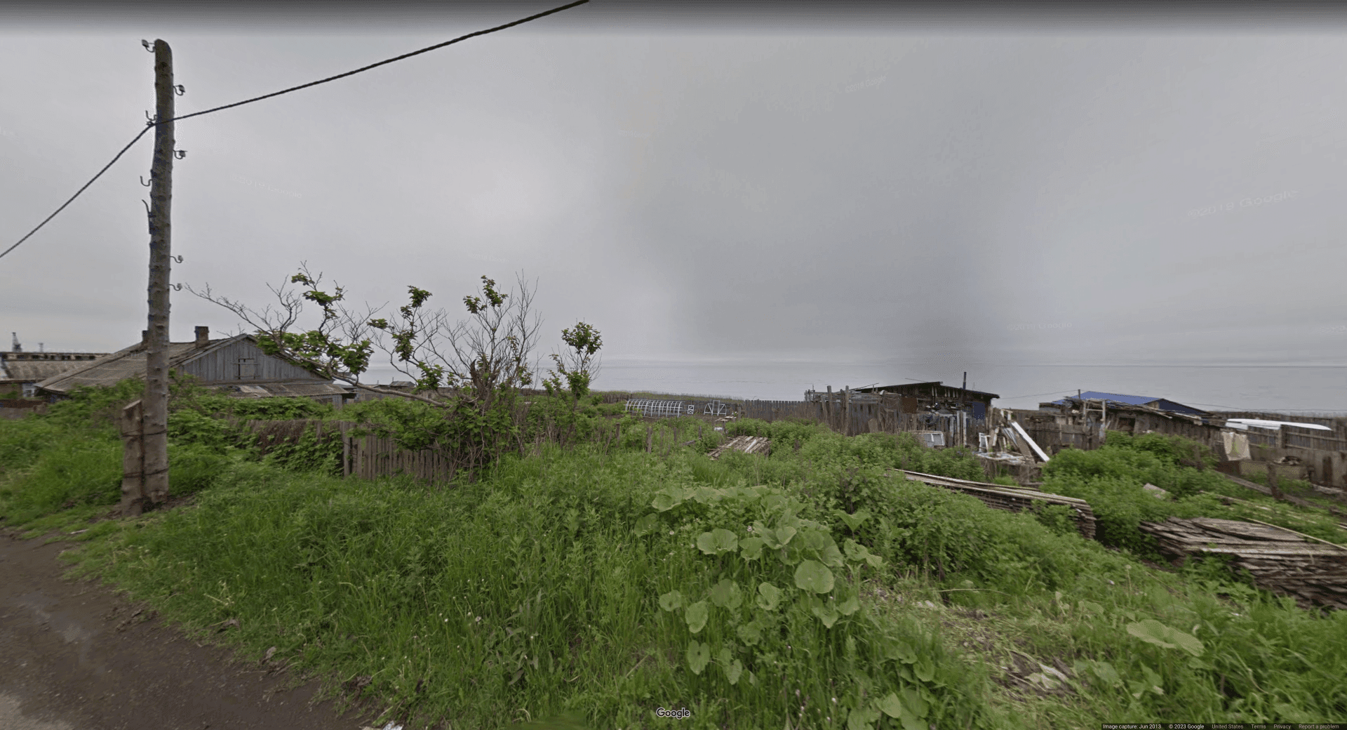 Image of dilapidated sheds and fences next to an ocean, with overcast skies